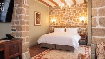 Une chambre avec un mur en pierre, un lit, une table de chevet, une télévision, un bureau et une chaise.