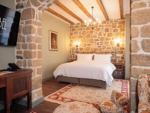 A bedroom with a stone wall, a bed, a nightstand, a TV, a desk, and a chair. - Vila Ebel Hotel Pool & Spa (Korçë)