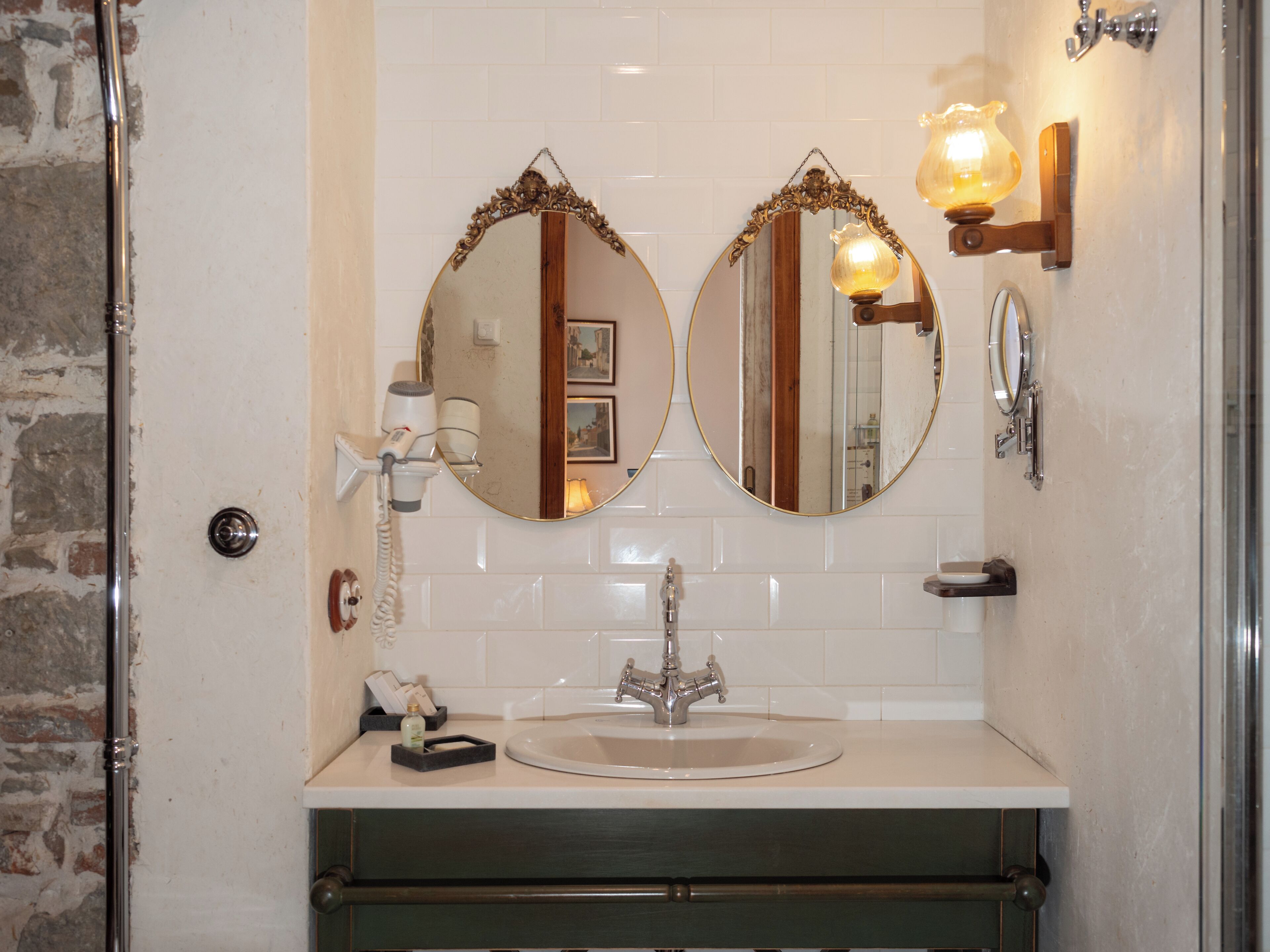 A bathroom with a sink, two mirrors, a hairdryer, and a light fixture.