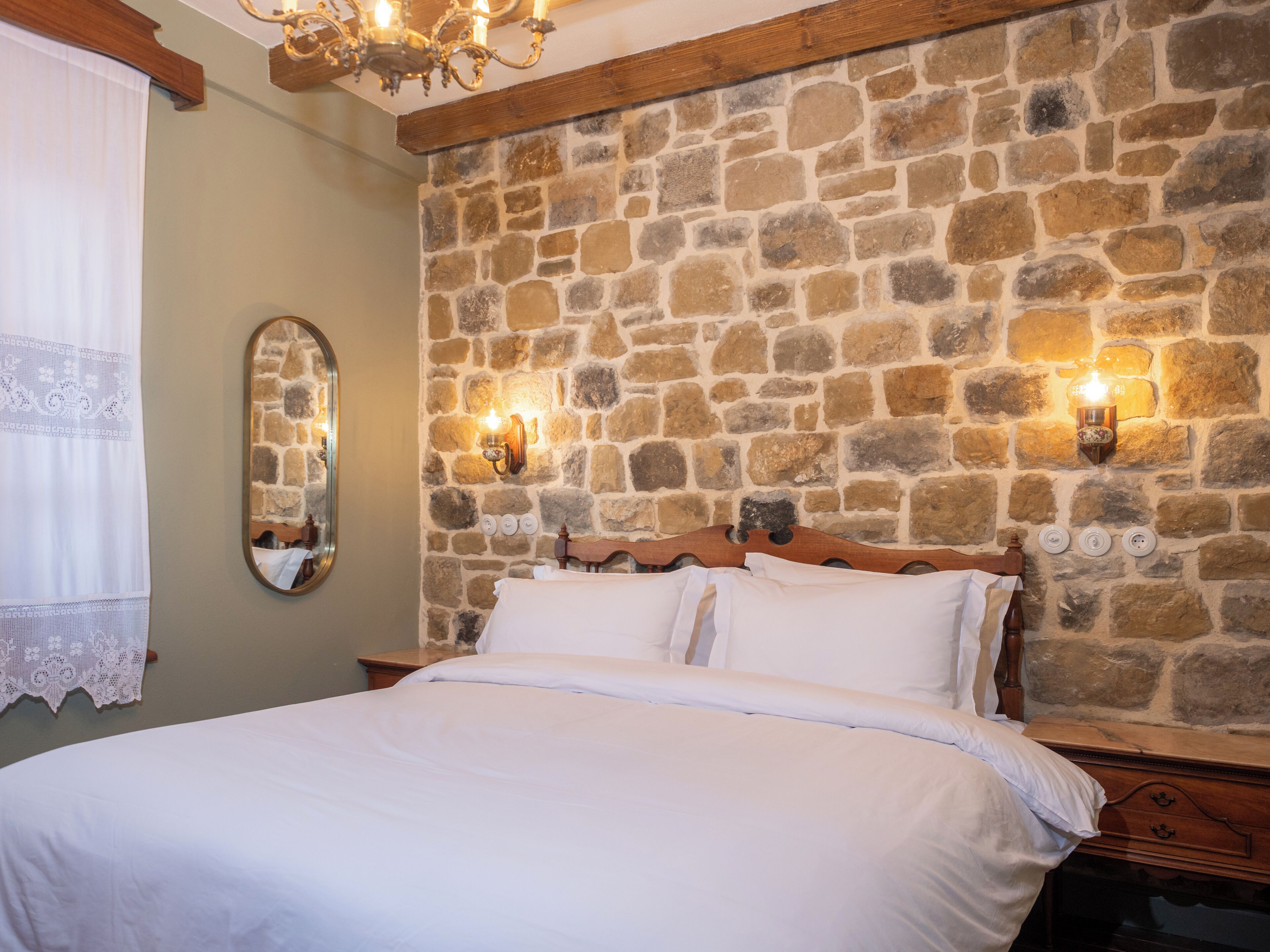 Un dormitorio con pared de piedra, estructura de cama de madera y dos lámparas fijadas a la pared.