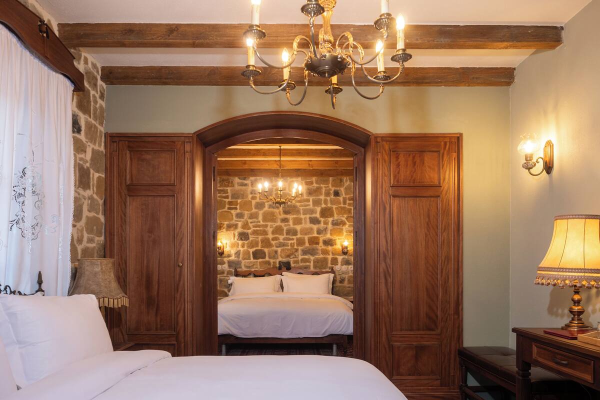 Ein Schlafzimmer mit einem großen Bett, einem Holzschrank, einer Steinwand, einer Deckenleuchte und einem Schreibtisch mit Lampe.