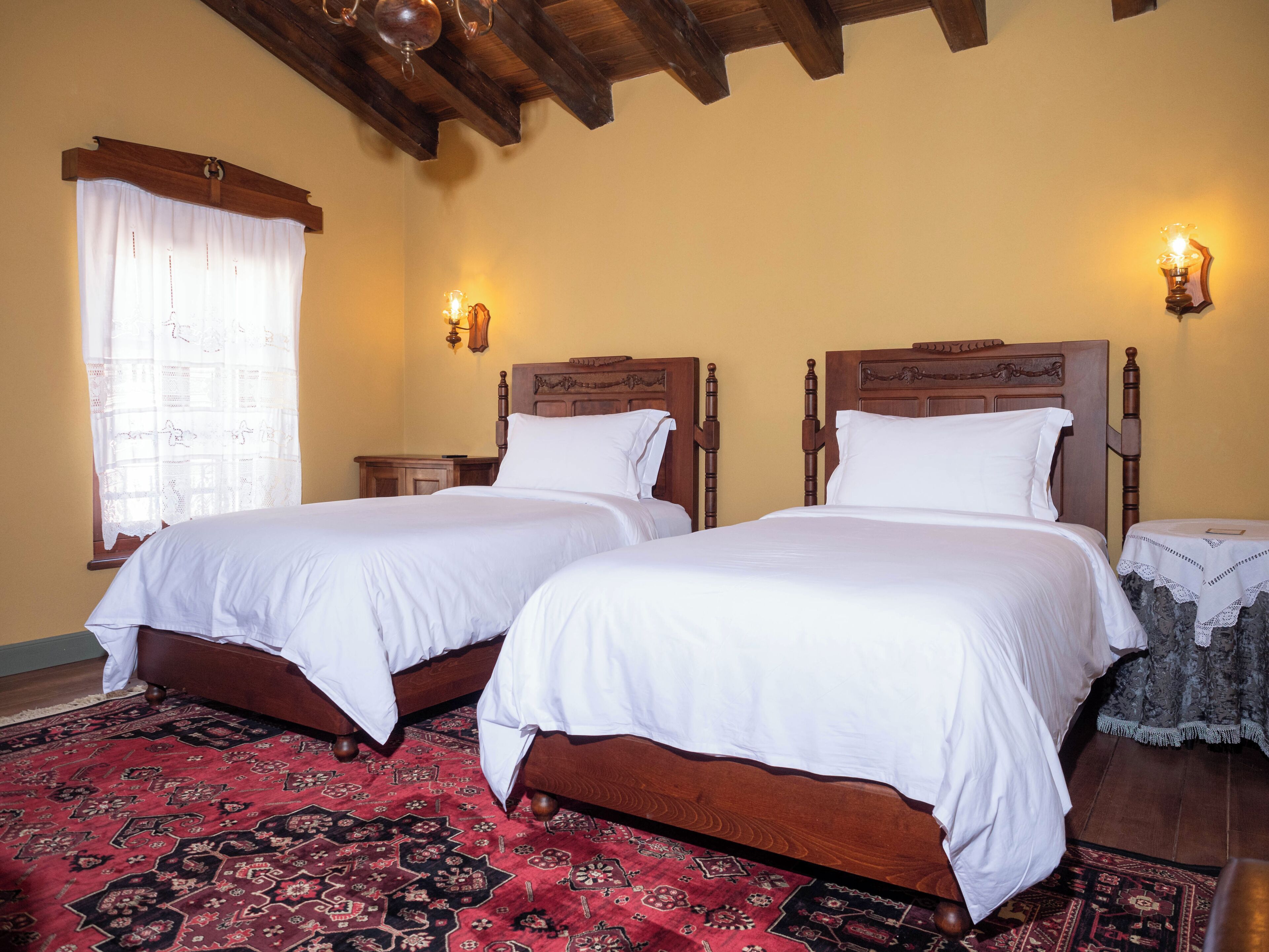 A room with two wooden beds, a red patterned carpet, and a window with a white curtain.