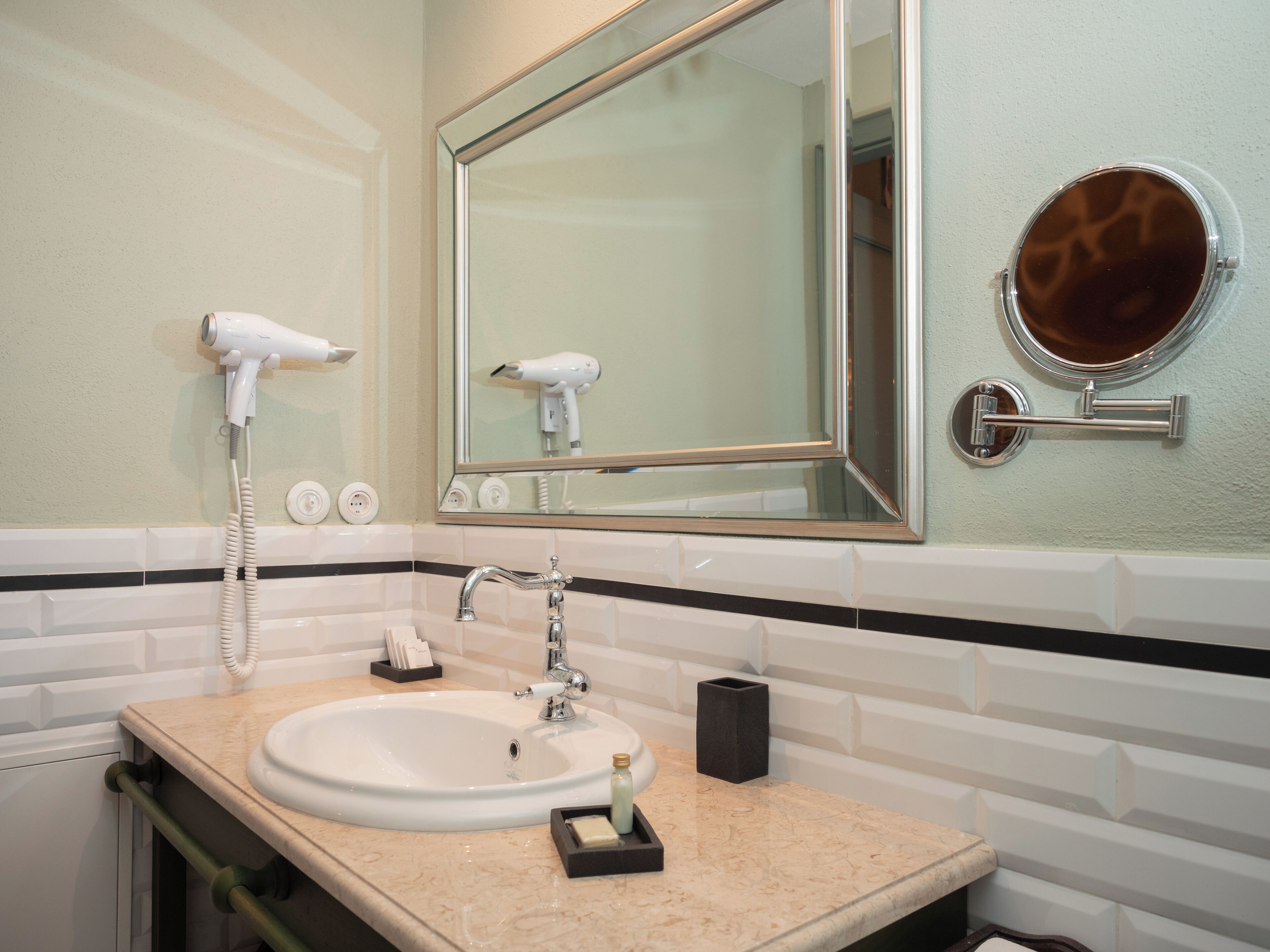 A bathroom with a sink, mirror, hairdryer, and a round mirror on the wall.
