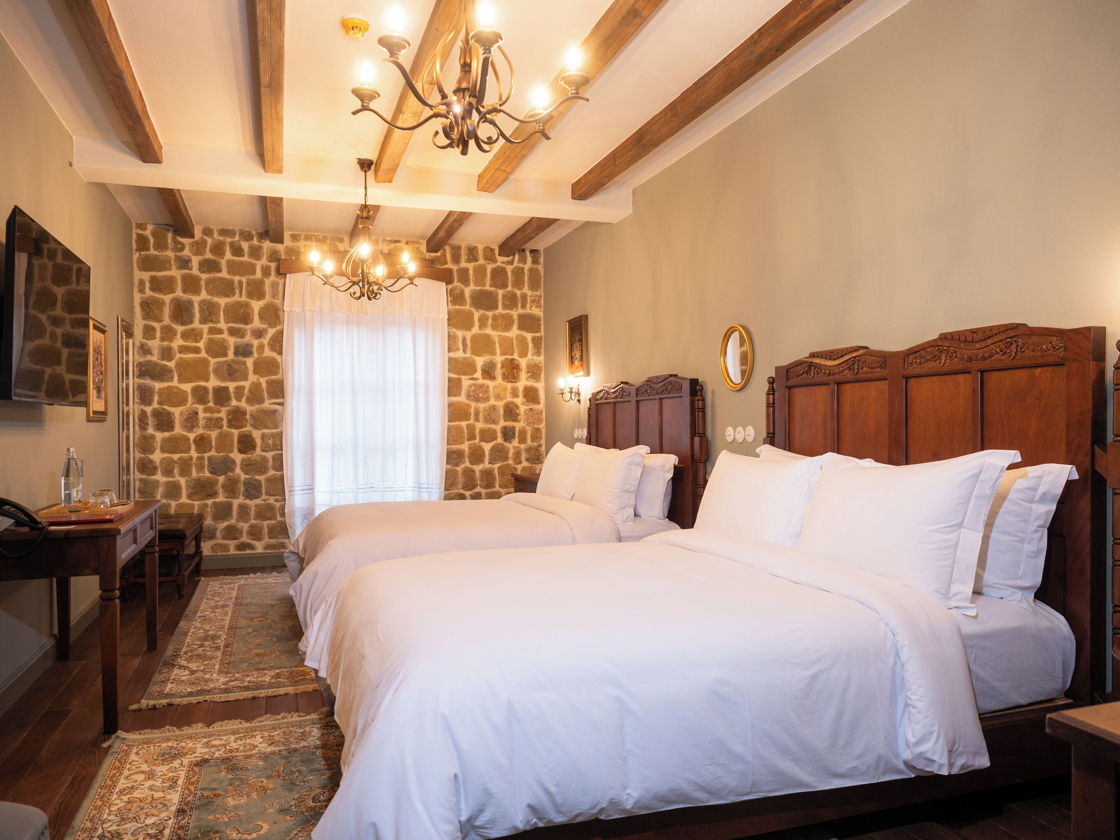 A hotel room with two beds, a stone wall, a chandelier, and a wooden headboard.