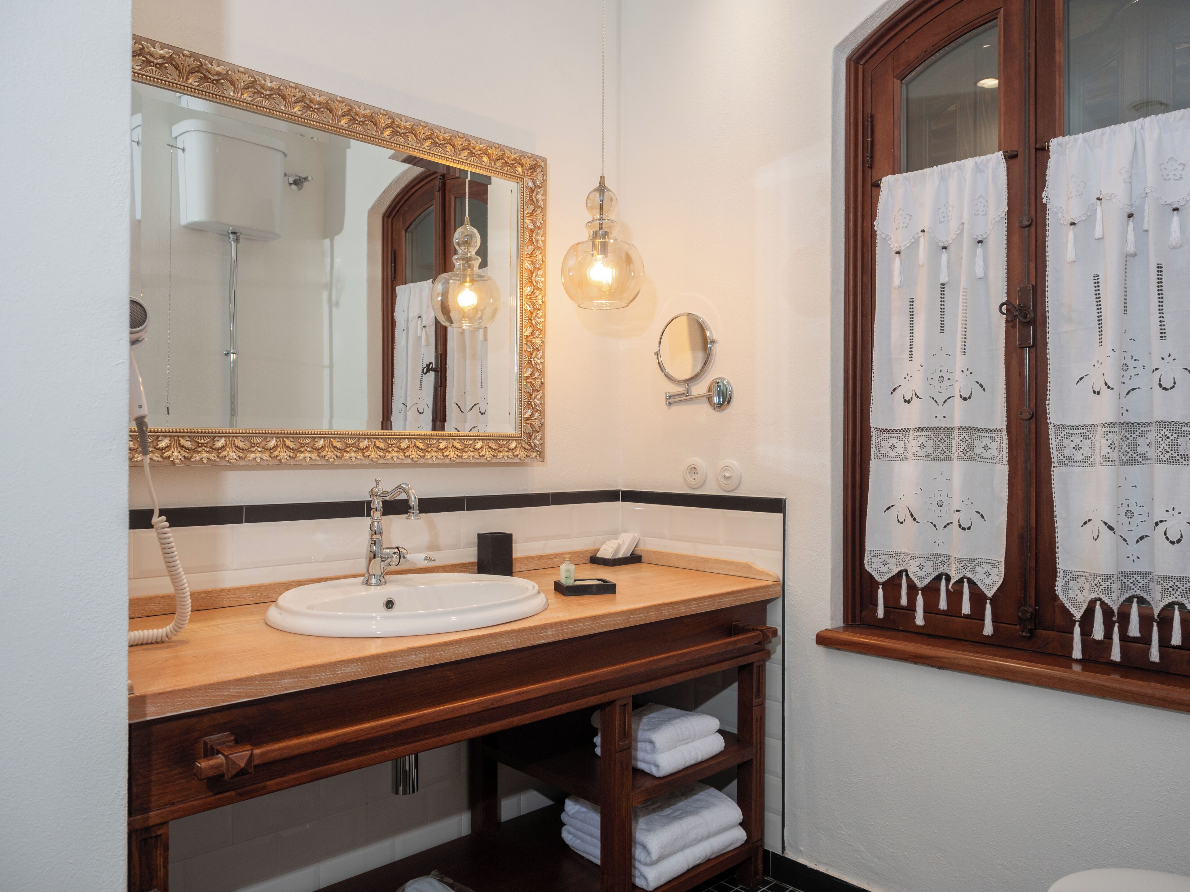 A bathroom with a wooden vanity, a large mirror, a sink, and a window with curtains.