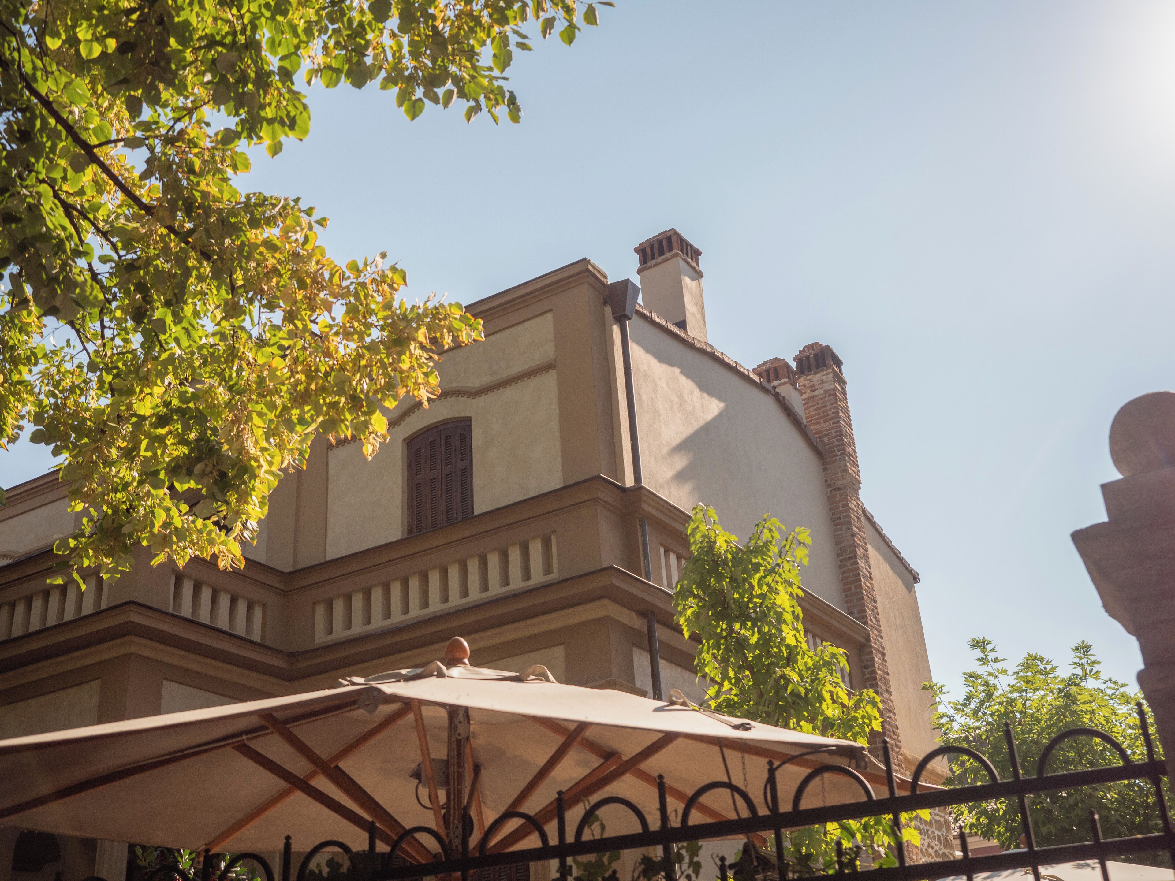 A building with a classical architectural style, featuring a prominent chimney, a balcony with a railing, and a large umbrella in the foreground.