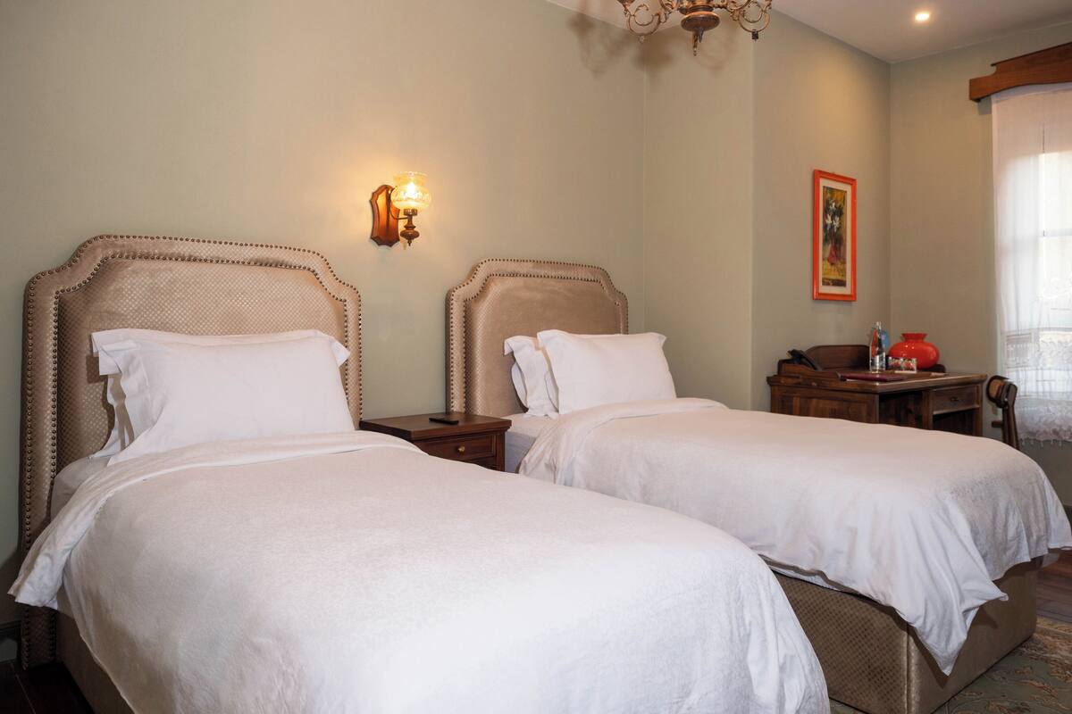 Ein Hotelzimmer mit zwei Betten, einer Kristallleuchtre, einem Nachttisch mit Lampe und einem Gemälde an der Wand.