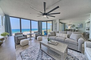 A spacious living room with a large window overlooking the beach, a ceiling fan, and a modern kitchen area. - Tower 2-202 Edgewater Beach Resort-Sleeps 8! (Panama City Beach)