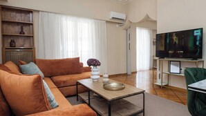 A living room with a sofa, a coffee table, a TV, and a bookshelf. - Neos Kosmos Gem w Acropolis View Balcony (Athens)