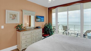 A hotel room with a large bed, a dresser, a mirror, a television, and a balcony with a view of the beach. - Lighthouse 506 by Liquid Life (Gulf Shores)