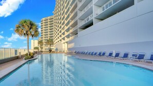 A swimming pool with lounge chairs, a palm tree, and a tall building in the background. - Lighthouse 506 by Liquid Life (Gulf Shores)