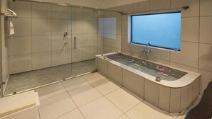 A modern bathroom with a glass-enclosed shower, a freestanding bathtub with a flower arrangement, and a window providing natural light. - The Stay Ranakpur (Desuri)