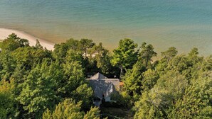 A coastal house surrounded by dense green trees, with a clear view of the ocean. - Lakeside Home with Panoramic Views of Lake Michigan! (Harbor Springs)