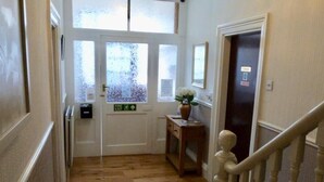 A hallway with wooden flooring, a fire exit sign, a small table with a vase, and a door with a security lock. - The Beacon Hotel (Redcar)