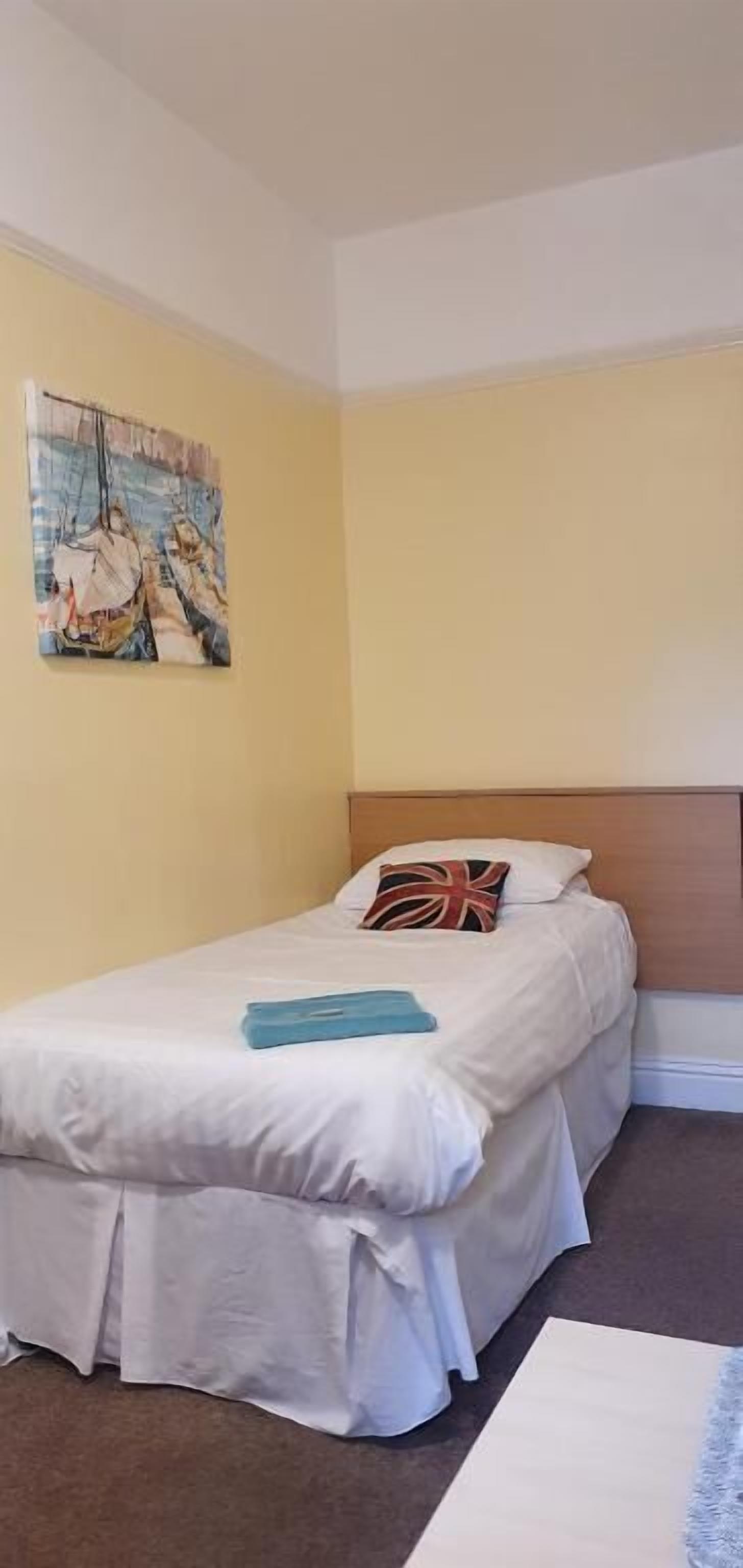 A single bed with a headboard, a pillow with a Union Jack design, and a painting of a woman on a swing.
