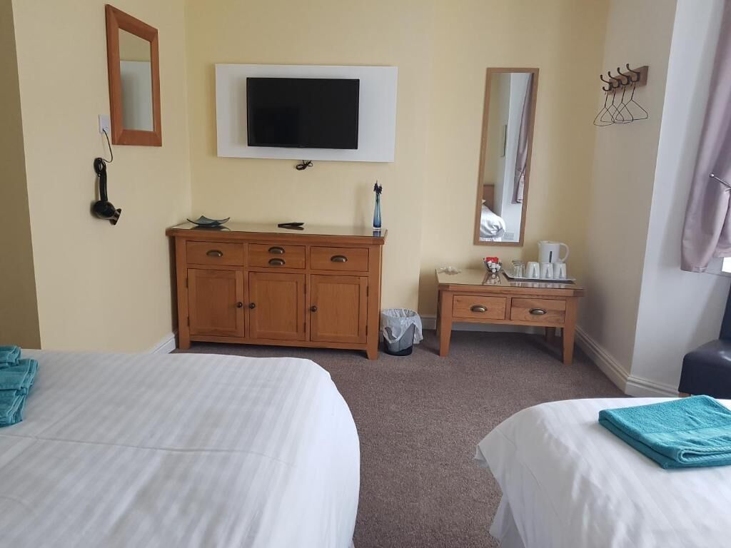 Ein Hotelzimmer mit zwei Betten, einem Holzschrank, einem Fernseher, einem Spiegel und einem kleinen Tisch mit einer Kaffeemaschine.
