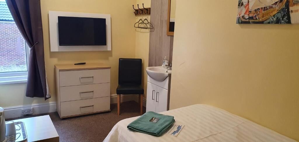 A hotel room with a bed, a desk, a chair, a TV, a sink, and a window with curtains.