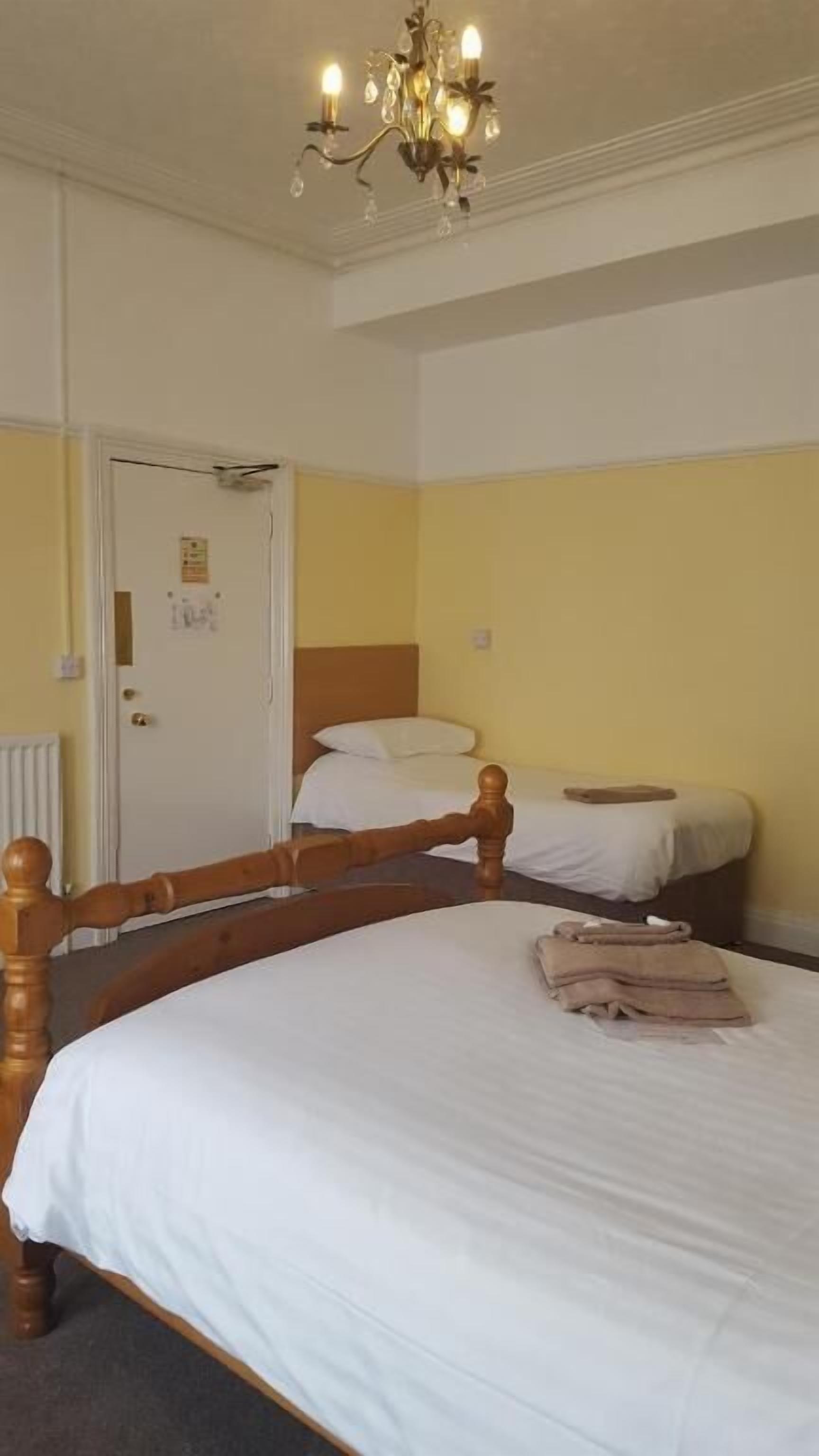 A hotel room with a large bed, a smaller bed, a wooden headboard, a chandelier, and a door with a sign.