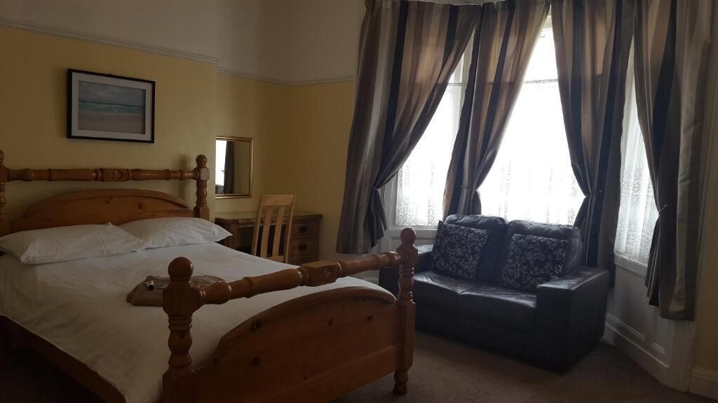 Une chambre à coucher avec un lit en bois, un canapé, une chaise, un miroir et une fenêtre avec des rideaux.