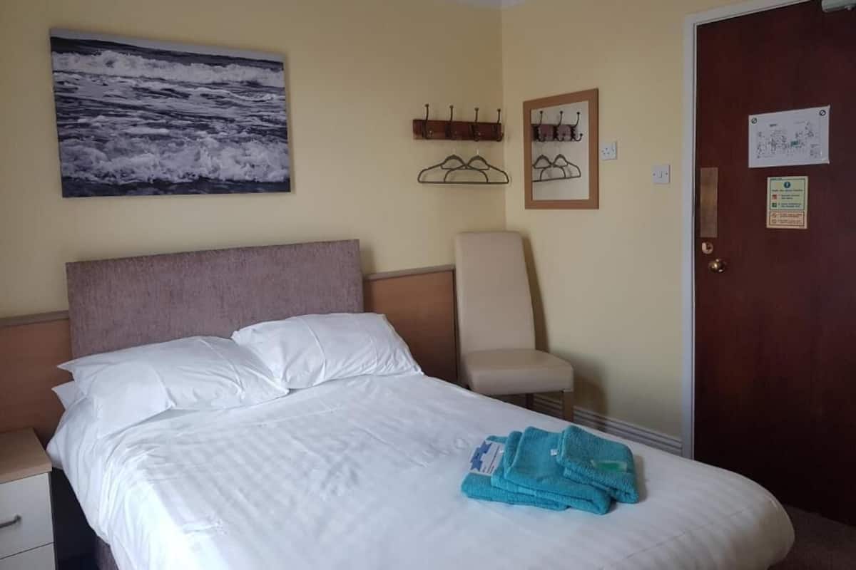 Una habitación de hotel con una cama, una silla, un perchero y una puerta con un aviso.