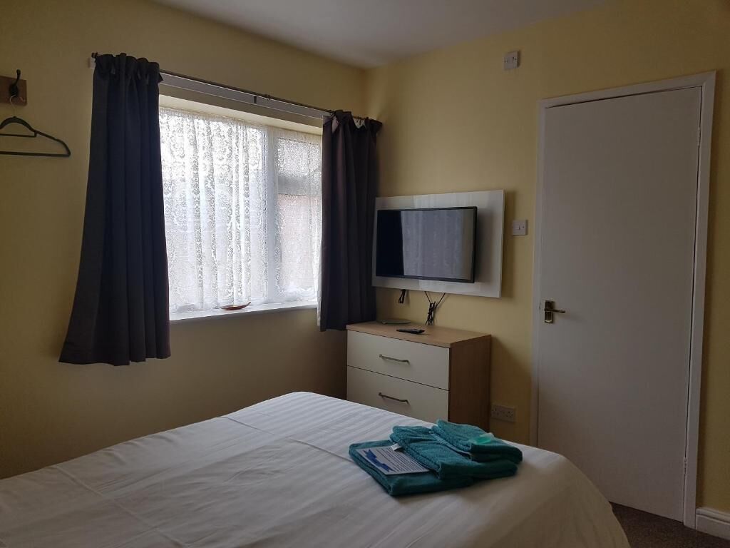 Een slaapkamer met een bed, een televisie op een dressoir, een raam met gordijnen en een deur.