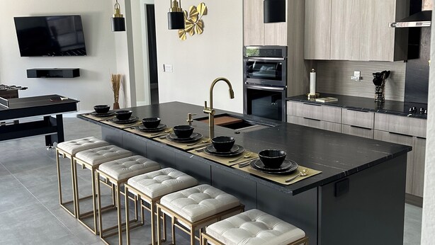 Een moderne keuken met een centraal kookeiland, barstoelen, een flatscreen televisie en inbouwapparatuur.