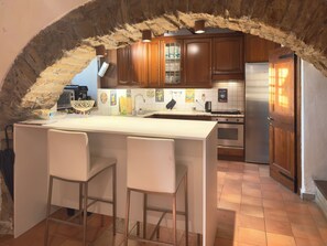 A kitchen with a stone arch, wooden cabinets, a stainless steel refrigerator, and a bar area with stools. - "Fortuna del Lupo" Vacation Apartment for Tuscany Lovers (Subbiano)