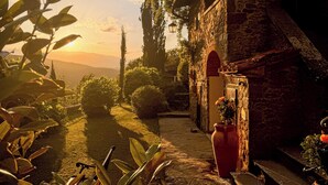 Un bâtiment en pierre avec un chemin menant à une porte, entouré de verdure et sous un ciel dégagé.
