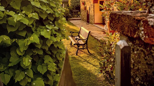 Un bâtiment en pierre avec une arche rouge, un banc et une végétation luxuriante.