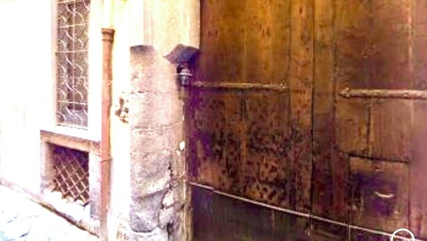 Una puerta grande de madera con un picaporte metálico y un detalle decorativo de metal encima.