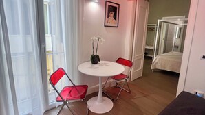 Una habitación moderna con una mesa redonda blanca, dos sillas rojas, un reposapiés negro, una lámpara colgante roja, un cuadro en la pared y un equipo de aire acondicionado.