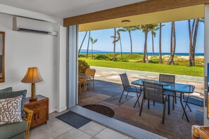 Ein Zimmer mit Glastür, die auf eine Terrasse mit Tisch, Stühlen, einer Lampe und einer Couch führt.