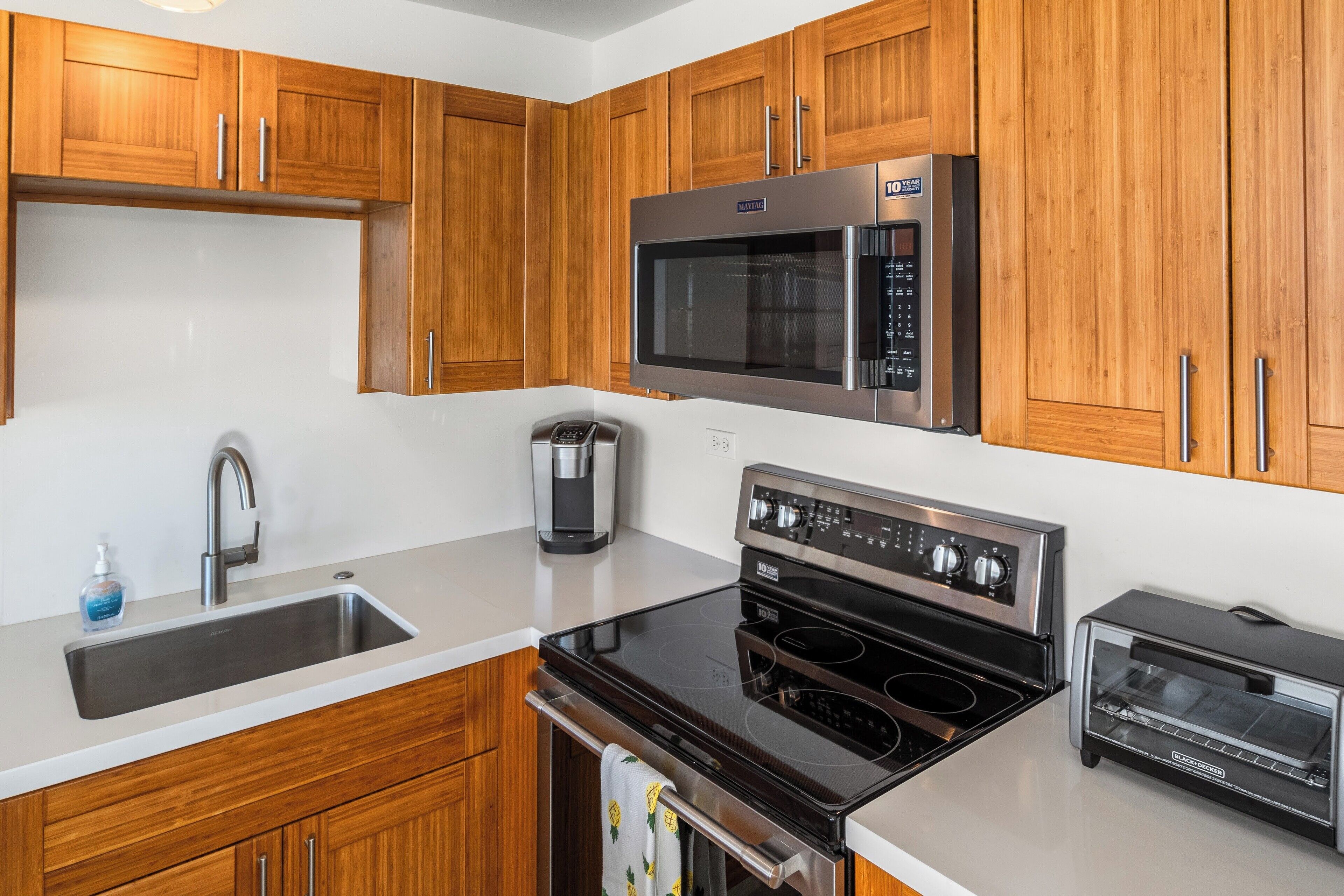 Una cocina moderna con armarios de madera, un microondas de acero inoxidable, un horno empotrado, una hornalla y un tostador.