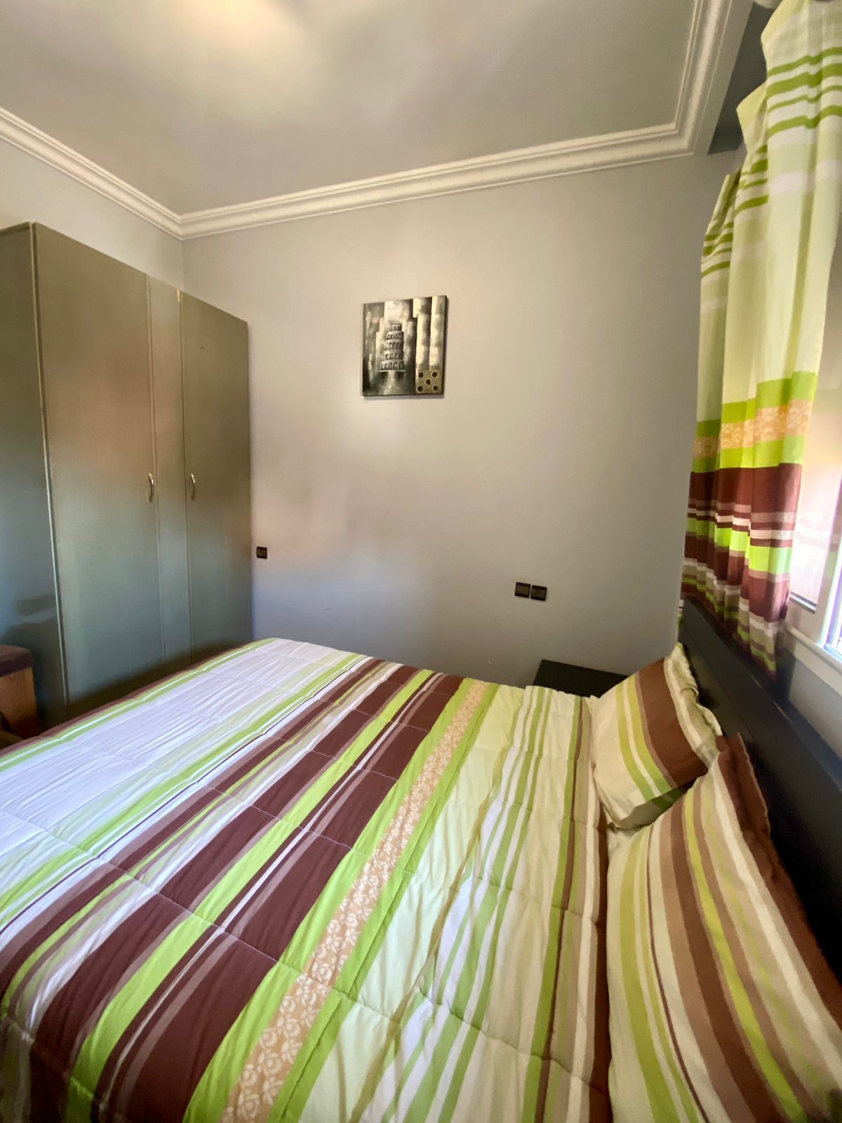Habitació amb llit, armari i finestra amb cortines.