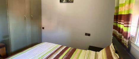 Habitació amb llit, armari i finestra amb cortines.