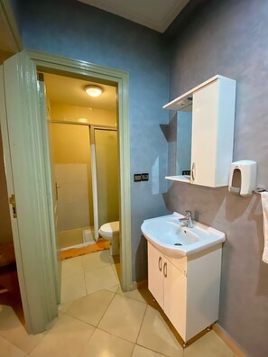 Une salle de bain avec un lavabo blanc, un miroir et des toilettes, une porte de douche et une serviette accrochée au mur.