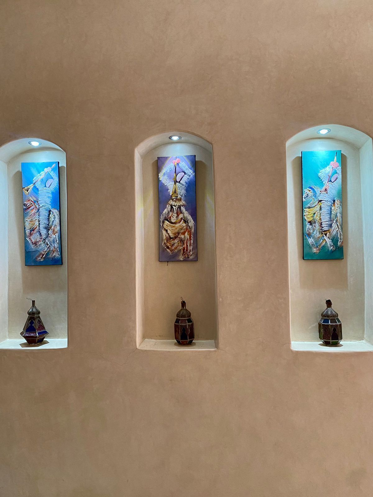 Drie aan de muur bevestigde schilderijen, met decoratieve vazen eronder.