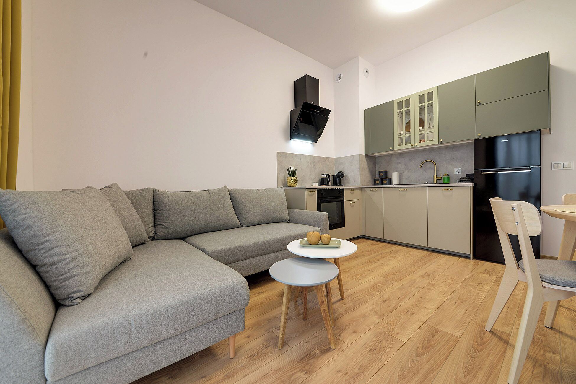 Een moderne woonkamer met een grijze bank, een klein rond tafeltje en een houten vloer.