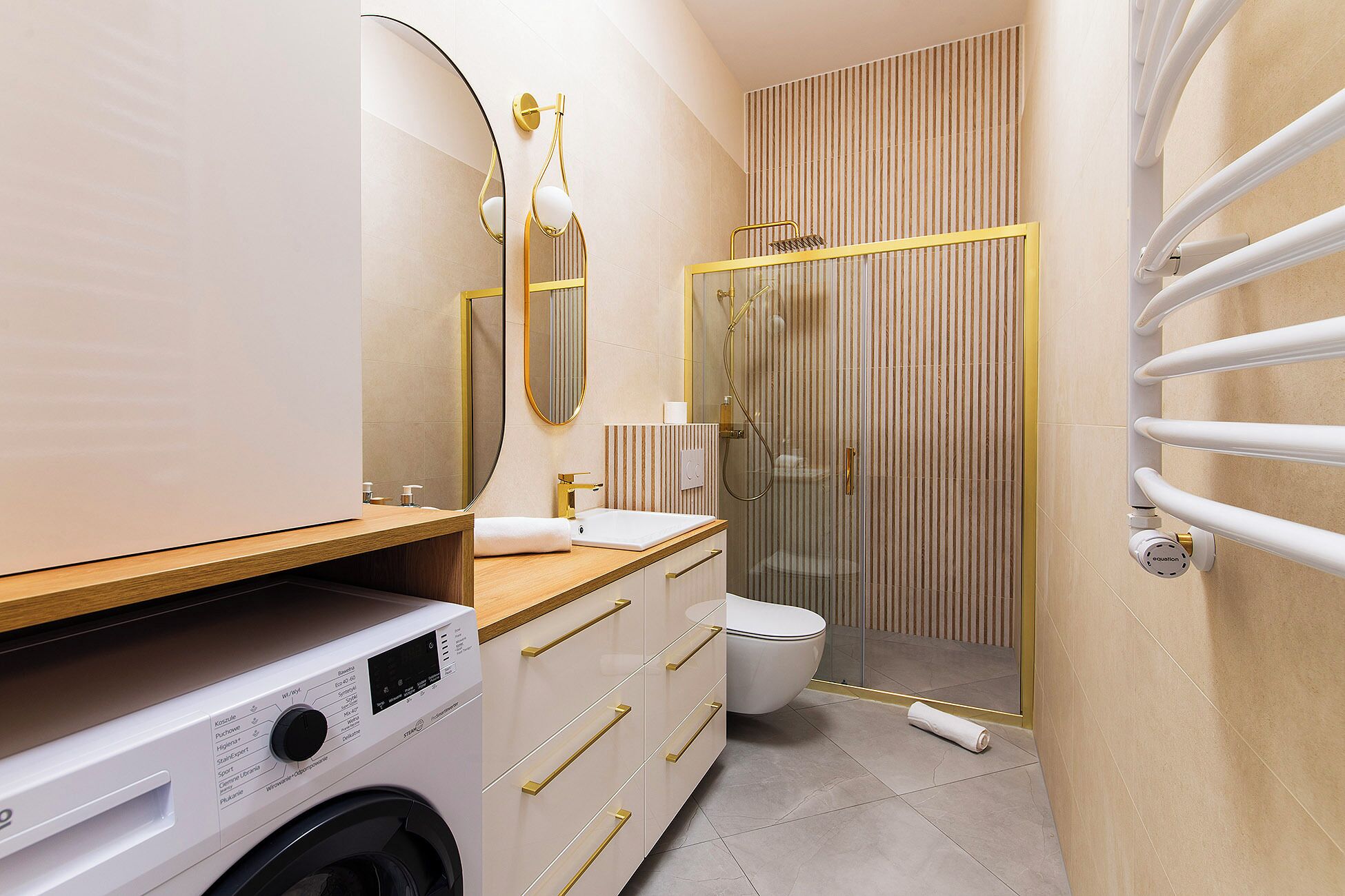 Une salle de bain moderne équipée d’un lave-linge, de toilettes et d’une douche séparée par une paroi en verre.