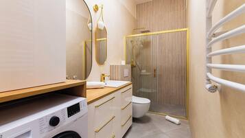 Une salle de bain moderne équipée d’un lave-linge, de toilettes et d’une douche séparée par une paroi en verre.