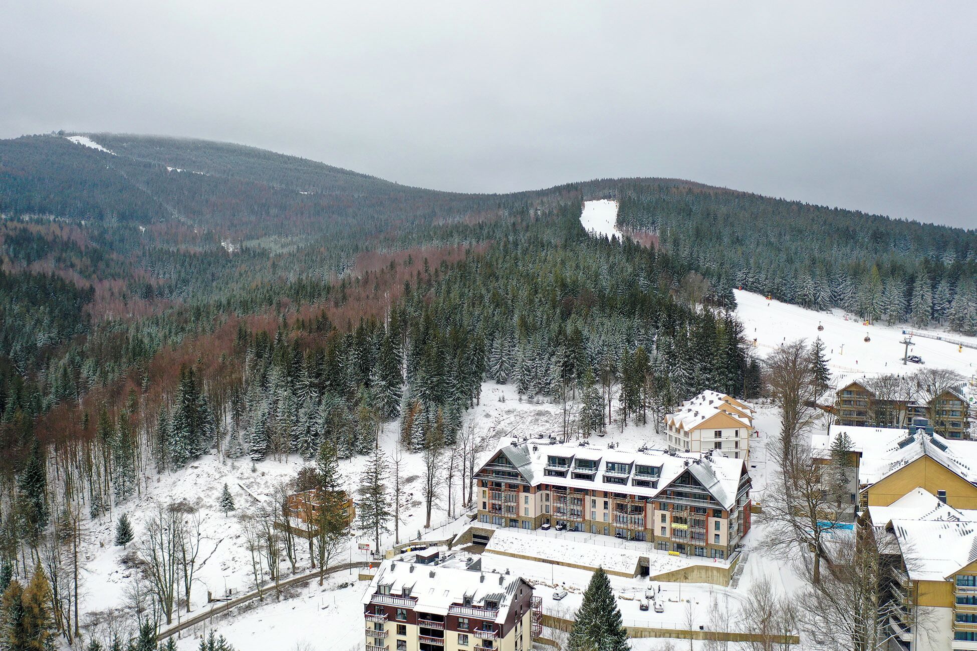 Montanha coberta de neve com estação de esqui, incluindo edifícios com varandas e um teleférico.