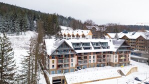 A modern ski resort building with multiple levels, large windows, and a ski lift in the background. - RentPlanet - Źródło Izery (Swieradow-Zdroj)
