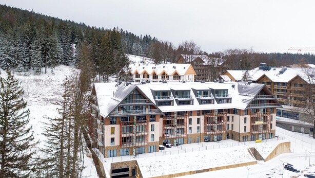 A modern ski resort building with multiple levels, large windows, and a ski lift in the background. - RentPlanet - Źródło Izery (Swieradow-Zdroj)