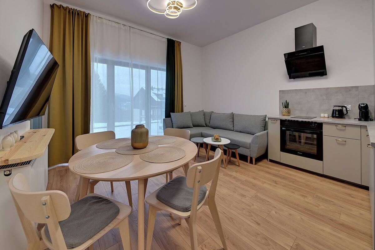 A modern living space with a dining area, sofa, kitchen, and a TV.