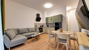 A modern living space with a grey sofa, a small round table, and a kitchen area with green cabinets. - RentPlanet - Źródło Izery (Swieradow-Zdroj)