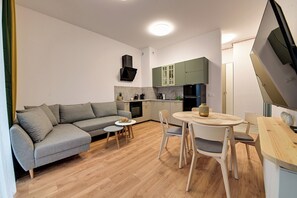 A modern living space with a grey sofa, a small round table, and a kitchen area with green cabinets. - RentPlanet - Źródło Izery (Swieradow-Zdroj)
