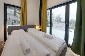 A hotel room with a large bed, two bedside tables, a window with curtains, and a view of a snowy outdoor area. - RentPlanet - Źródło Izery (Swieradow-Zdroj)