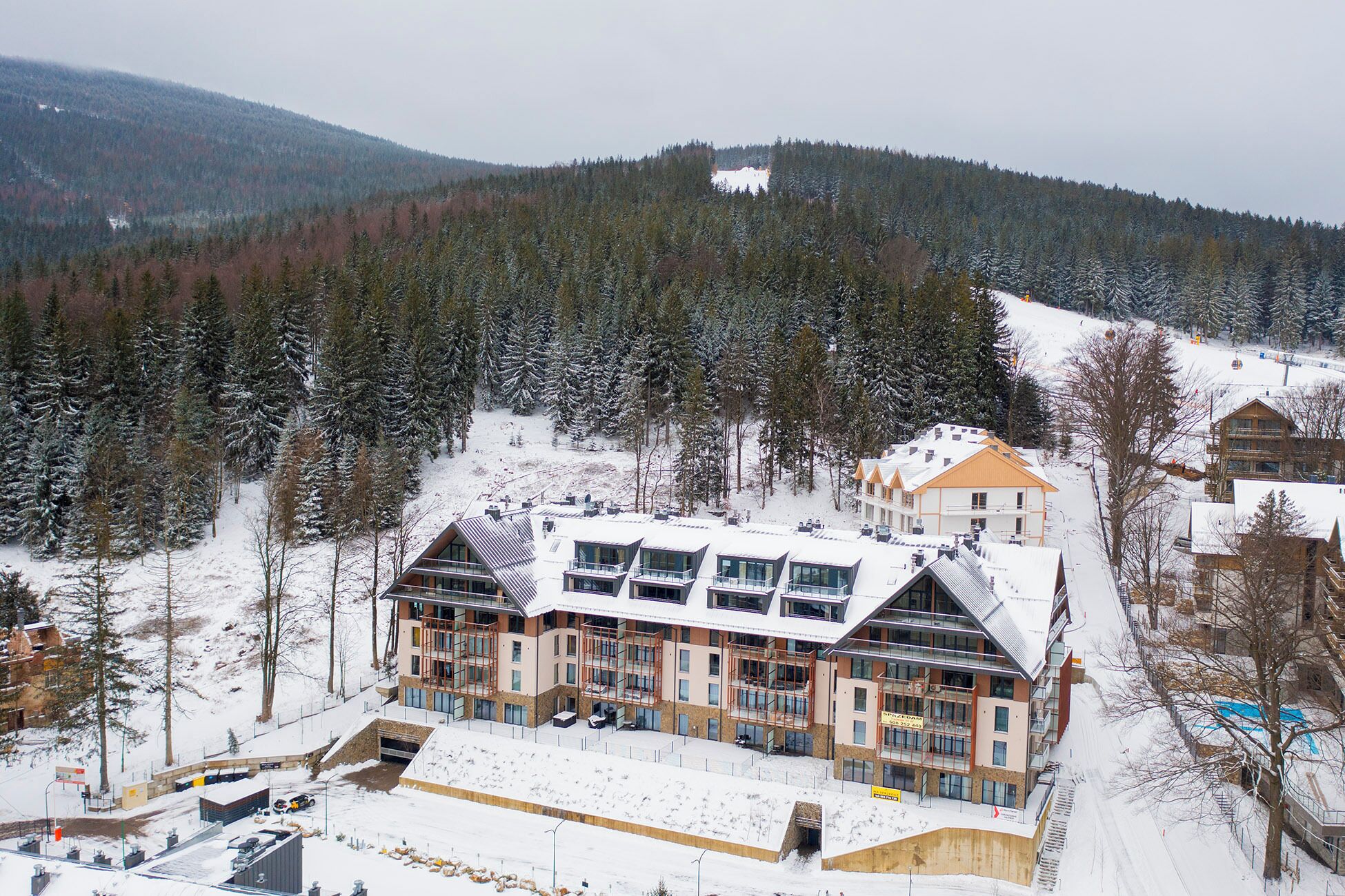 A modern hotel with multiple floors, large windows, and a ski slope in the background.