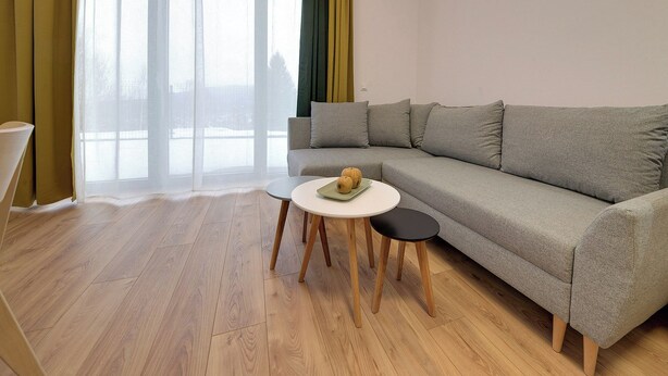 A modern living room with a grey sofa, a round white table, and a small black stool. - RentPlanet - Źródło Izery (Swieradow-Zdroj)