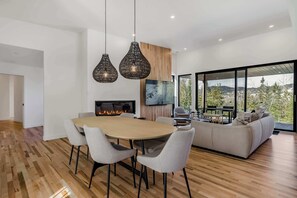 A modern living room with a wooden floor, a round dining table with chairs, a sofa, and a fireplace.